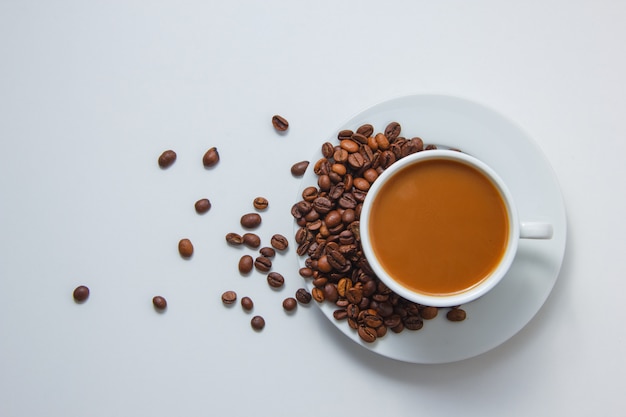 Vista superior de uma xícara de café com grãos de café em pires no fundo branco