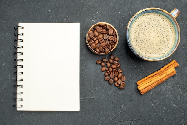 Vista superior de uma xícara de café com sementes de café canela em pau um caderno no fundo escuro isolado