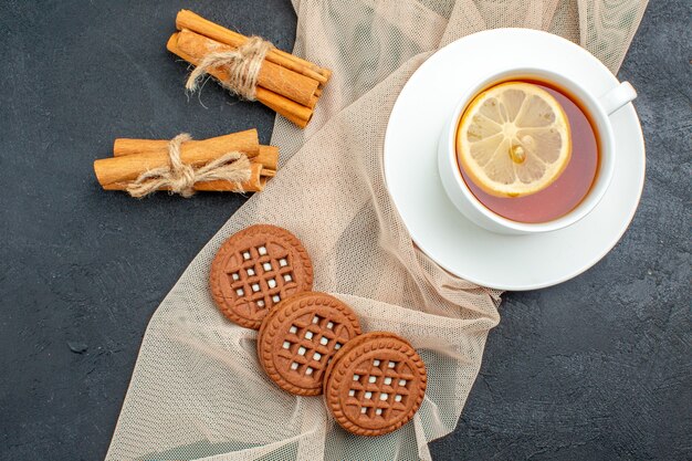 Foto grátis vista superior de uma xícara de chá com biscoitos de limão e canela em um xale bege na superfície escura