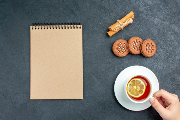 Vista superior de uma xícara de chá com bloco de notas de biscoitos de limão em paus de canela na superfície escura