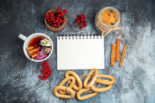 Vista superior de uma xícara de chá com cranberries vermelhas e biscoitos na superfície escura