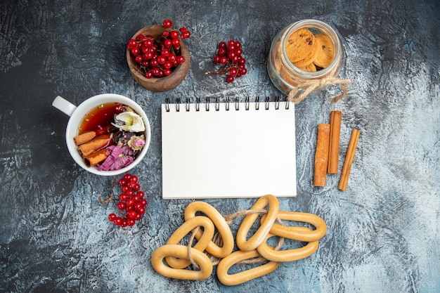 Vista superior de uma xícara de chá com cranberries vermelhas e biscoitos na superfície escura