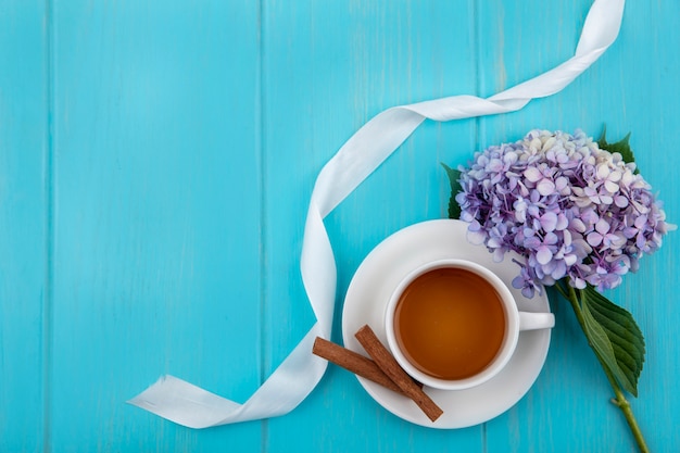 Vista superior de uma xícara de chá com paus de canela e lindas flores de gardenzia em um fundo azul de madeira com espaço de cópia