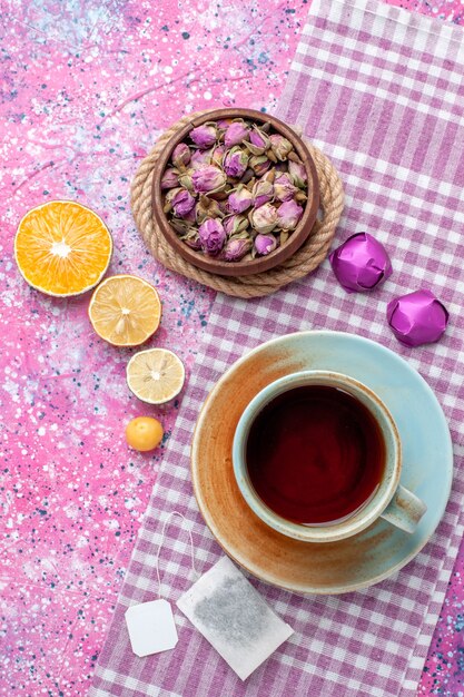 Vista superior de uma xícara de chá com rodelas de laranja e doces na superfície rosa