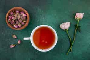 Foto grátis vista superior de uma xícara de chá com rosas claras e botões de rosa secos em uma tigela sobre uma superfície verde