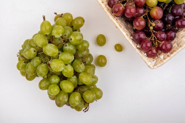 Vista superior de uvas brancas e uvas vermelhas em uma cesta no fundo branco