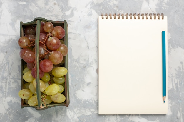 Vista superior de uvas frescas com bloco de notas no fundo branco.