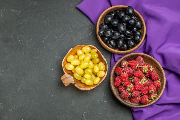 Foto grátis vista superior de uvas pretas e amarelas de framboesas em taças xale roxo na superfície escura e isolada no espaço livre