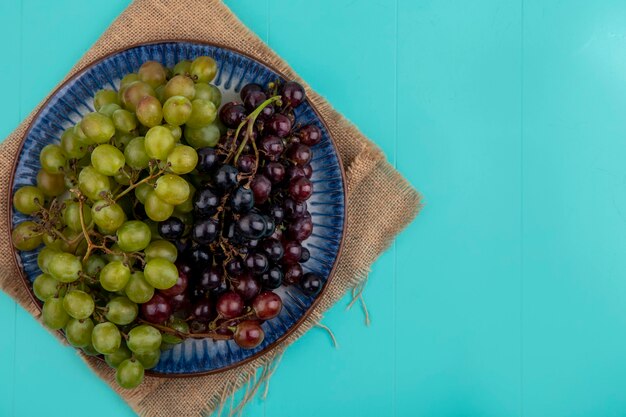 Vista superior de uvas pretas e brancas em prato e saco sobre fundo azul com espaço de cópia