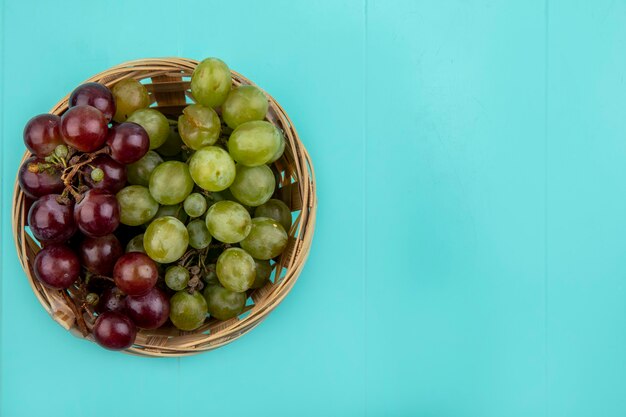 Vista superior de uvas vermelhas e brancas em uma cesta em fundo azul com espaço de cópia