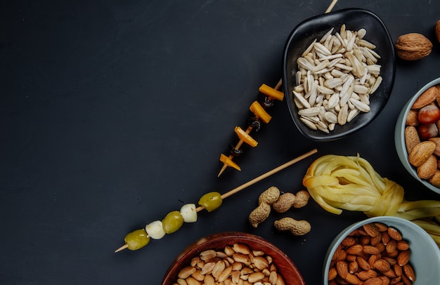 Vista superior de variados petiscos de cerveja sementes de girassol amendoins em conserva azeitonas e queijo de corda no preto com espaço de cópia