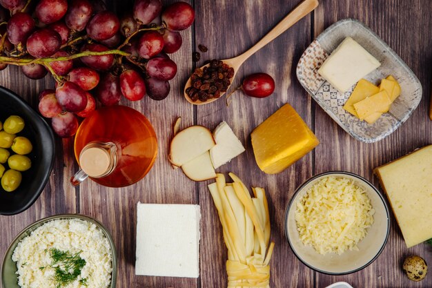 Vista superior de vários tipos de queijo com mel em uma garrafa de vidro e uvas doces em madeira rústica