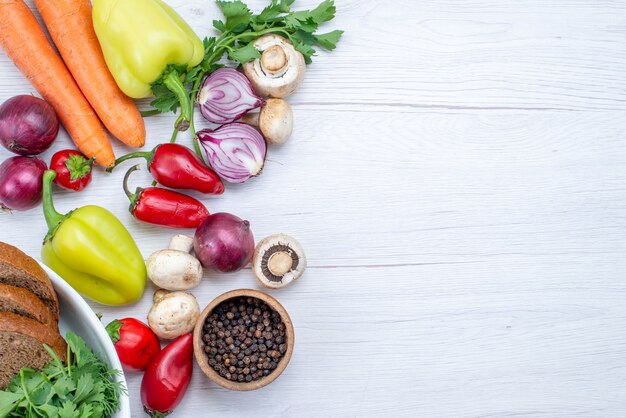 Vista superior de vegetais frescos, como pimenta, cenoura, cebola e pão em uma mesa leve, prato de vitaminas para refeição vegetal