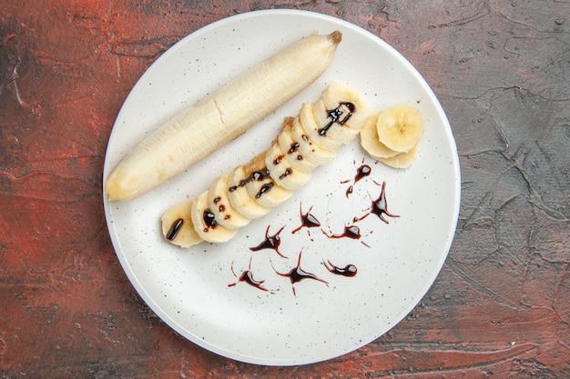 Vista superior deliciosa banana com pedaços fatiados dentro do prato no fundo escuro