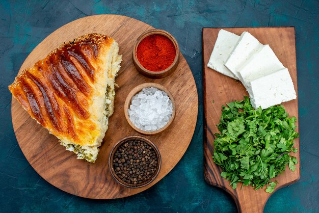 Vista superior deliciosa massa assada fatiada com recheio de verdes com temperos e queijo branco na mesa escura.