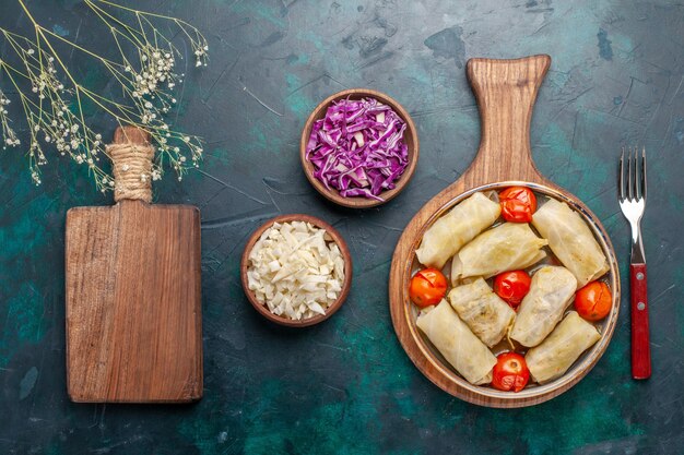 Vista superior deliciosa refeição de carne dolma enrolada com repolho e tomate em fundo azul escuro comida comida jantar prato de legumes cozinhar