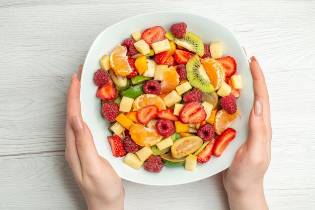 Vista superior deliciosa salada de frutas em fatias de frutas dentro do prato na cor branca vida saudável foto frutas maduras maduras