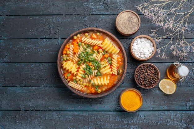 Vista superior deliciosa sopa de massa de macarrão espiral com temperos em molho de chão azul-escuro prato de cozinha sopa de massa italiana