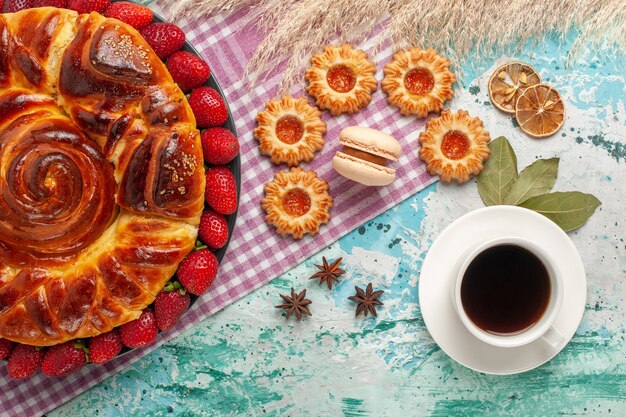 Vista superior deliciosa torta com morangos e xícara de chá na superfície azul