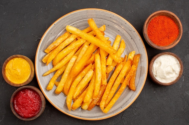 Vista superior deliciosas batatas fritas com temperos no fundo escuro prato de batata refeição hambúrguer fast-food