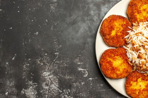 Vista superior deliciosas costeletas fritas com arroz cozido em uma refeição de prato de carne de superfície escura