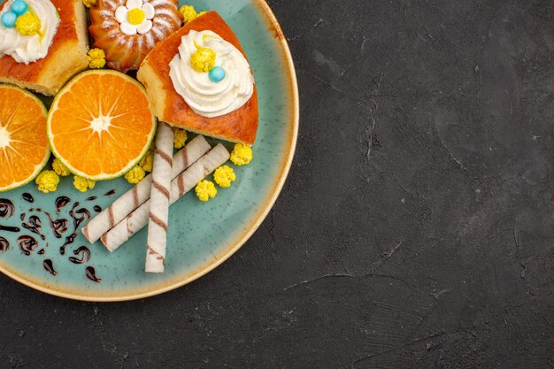 Vista superior deliciosas fatias de bolo com biscoitos de cachimbo e tangerinas fatiadas em fundo escuro torta de bolo de frutas biscoitos chá doce