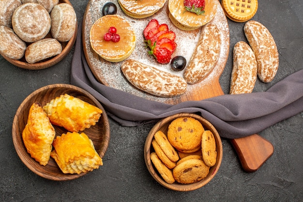 Vista superior deliciosas panquecas com frutas e bolos doces na mesa escura