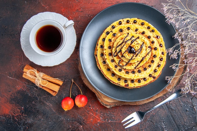 Vista superior deliciosas panquecas doces com uma xícara de chá na superfície escura