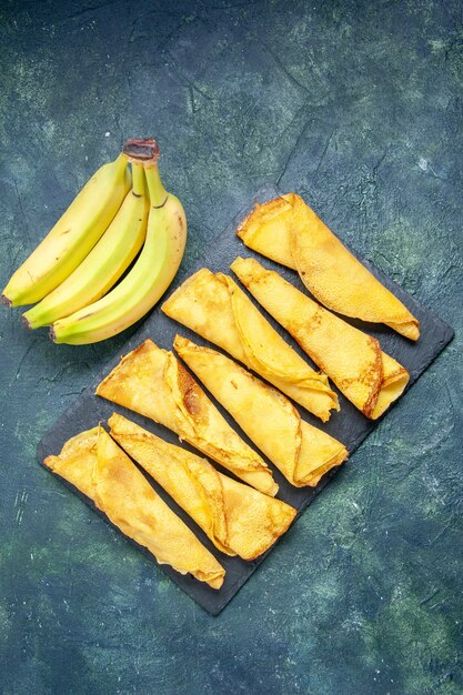 Vista superior deliciosas panquecas enroladas com bananas em fundo escuro