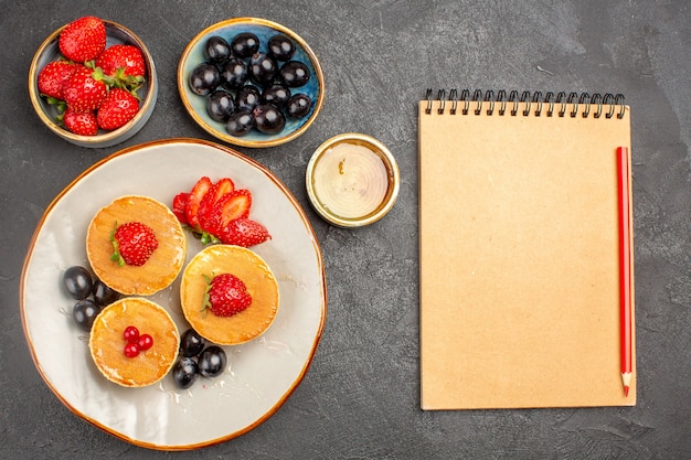 Vista superior deliciosas panquecas pouco formadas com frutas em torta de bolo de frutas com piso cinza