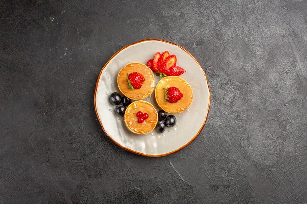 Vista superior deliciosas panquecas pouco formadas com frutas no escuro