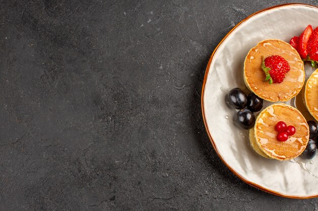 Vista superior deliciosas panquecas pouco formadas com frutas no escuro