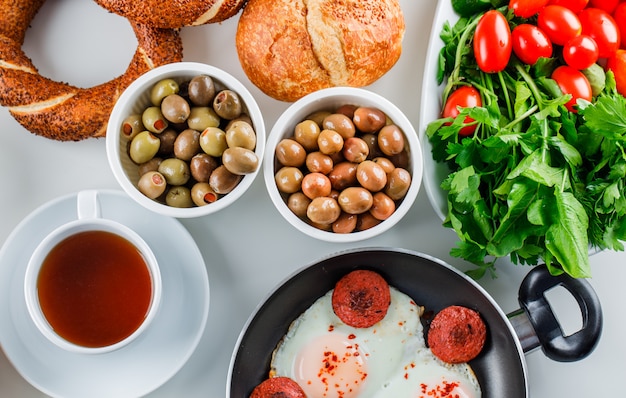 Vista superior deliciosas refeições em panela com uma xícara de chá, pão turco, tomate, verduras na superfície branca