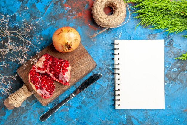 Vista superior deliciosas romãs na tábua de cortar faca de jantar um caderno no fundo abstrato azul