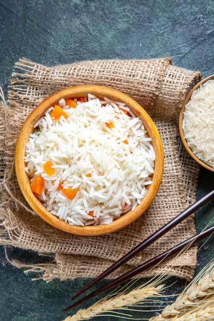Vista superior delicioso arroz cozido com arroz cru dentro de um pratinho na mesa escura