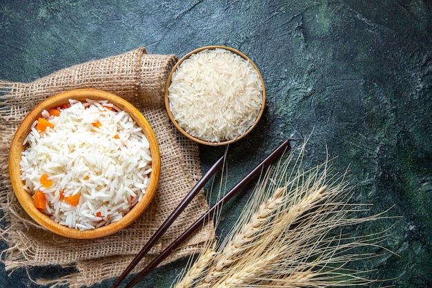 Vista superior delicioso arroz cozido com arroz cru dentro de um pratinho na mesa escura