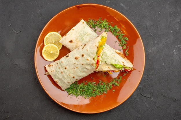 Vista superior - delicioso sanduíche de salada shaurma fatiado com rodelas de limão dentro do prato em um fundo escuro refeição de hambúrguer sanduíche de pão