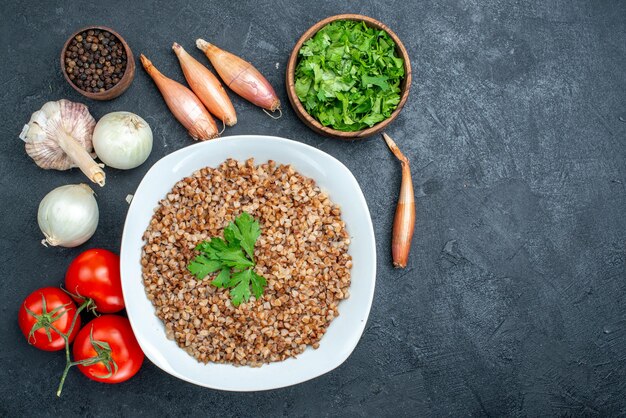 Vista superior delicioso trigo sarraceno cozido com tomates frescos e verduras no espaço cinza