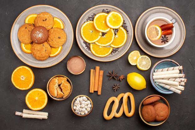 Vista superior deliciosos biscoitos com laranjas frescas e chá na superfície escura.