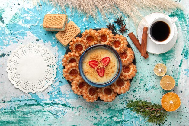 Vista superior deliciosos biscoitos de açúcar com waffles, xícara de café e sobremesa de morango na mesa azul