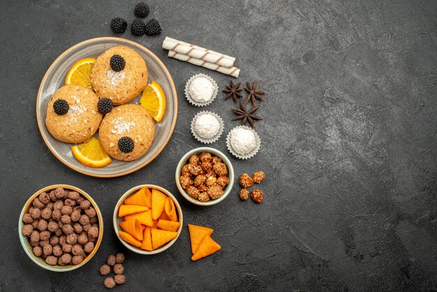 Vista superior deliciosos biscoitos de areia com batatas fritas e fatias de laranja na superfície escura.