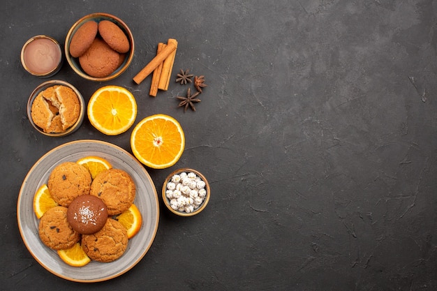 Vista superior deliciosos biscoitos de areia com fatias de laranjas frescas em fundo escuro biscoito de frutas biscoitos doces de cor cítrica de açúcar