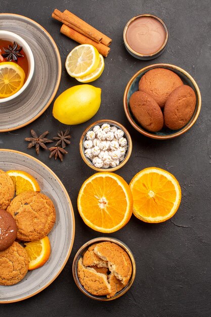 Vista superior deliciosos biscoitos de areia com laranjas frescas e uma xícara de chá no fundo escuro biscoito de frutas doce cítrico