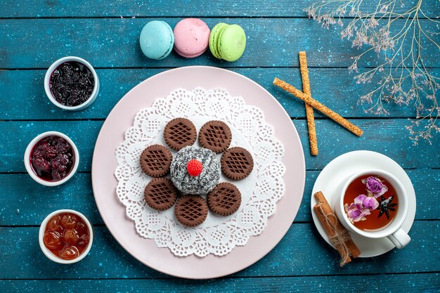 Vista superior deliciosos biscoitos de chocolate com geleia e xícara de chá na mesa rústica azul.