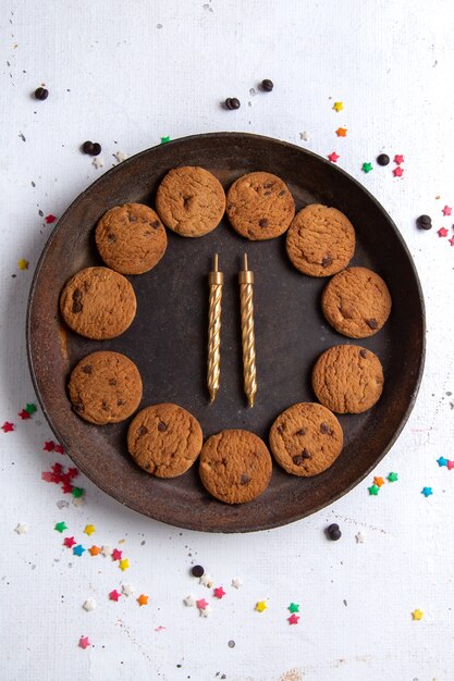 Vista superior deliciosos biscoitos de chocolate dentro de um prato redondo marrom com velas no fundo branco biscoito biscoito açúcar doce chá