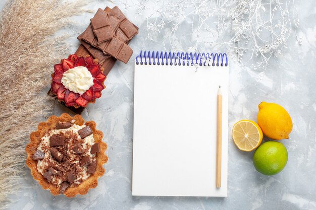 Vista superior deliciosos bolos cremosos com barras de chocolate e limão na mesa branca bolo biscoito doce açúcar