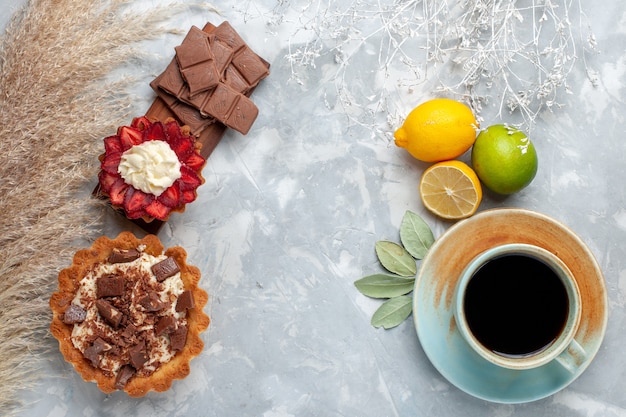 Vista superior deliciosos bolos cremosos com barras de chocolate, limão e chá na mesa branca bolo biscoito doce açúcar