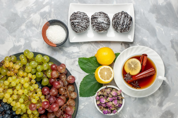 Vista superior deliciosos bolos de chocolate com chá de limão e uvas na superfície branca biscoito bolo de frutas doce açúcar