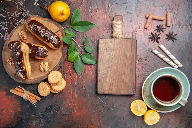 Vista superior deliciosos choco eclairs com uma xícara de chá na mesa escura sobremesa doce bolo