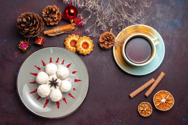 Vista superior deliciosos doces de coco com uma xícara de chá no fundo escuro chá doce biscoito bolo doce bombom